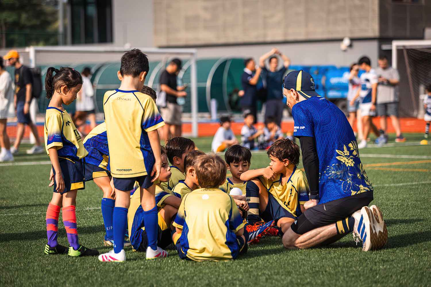 A Centaurs coach crouching at child height with a group of young Minis listening