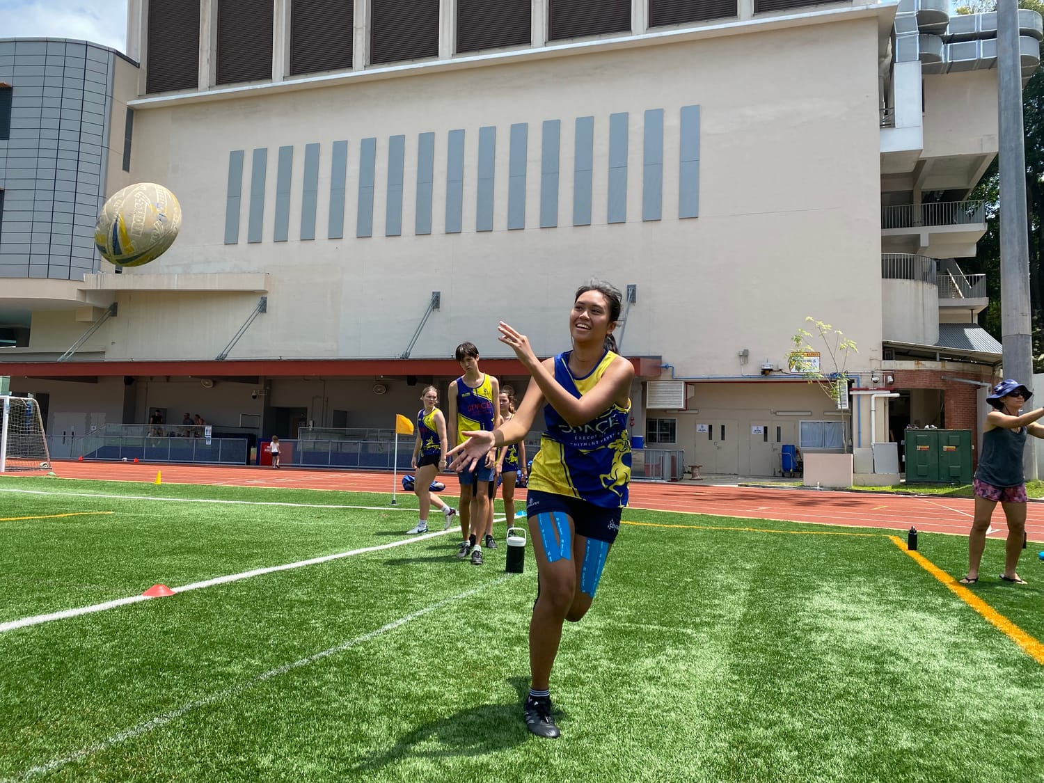 A Centaurs Touch player reaches up to catch a high pass, grinning, with teammates waiting their turn behind her